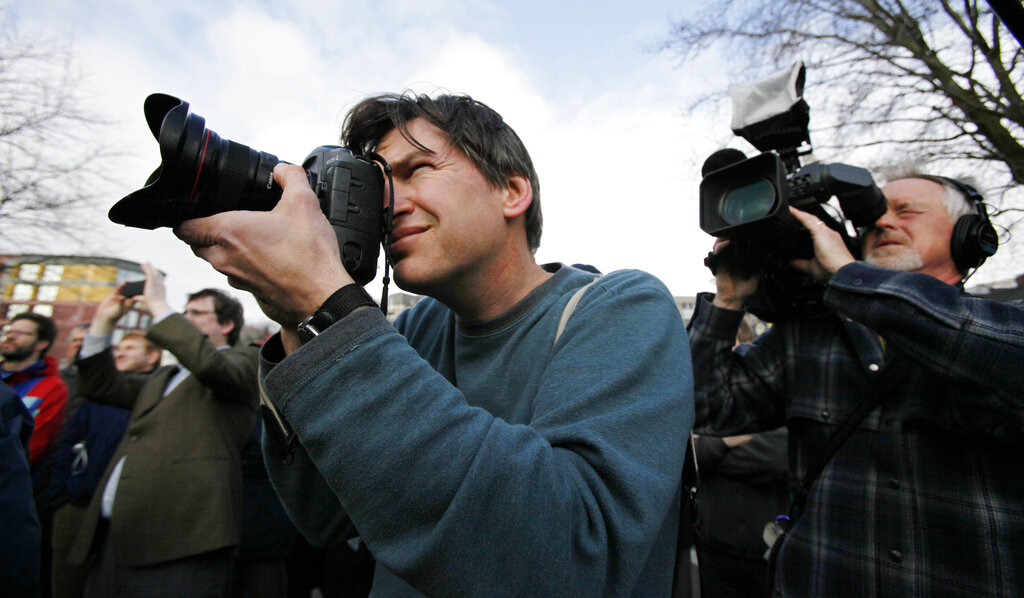 Two men hold cameras up to their eyes pointing out of frame.