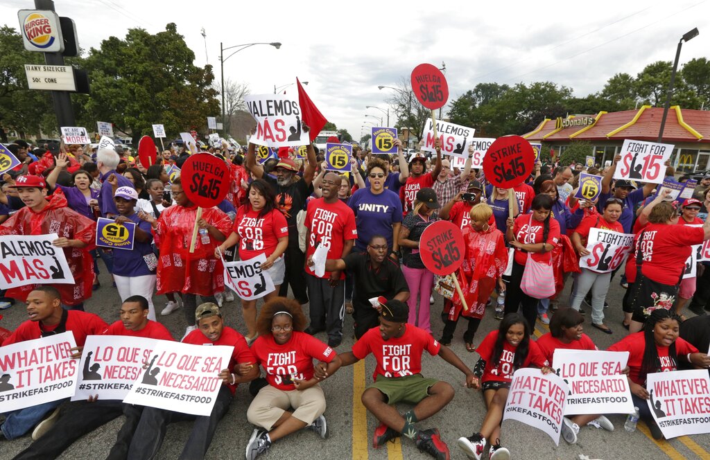 A large group of individuals in red shirts wearing shirts and holding signs with slogans calling for a fifteen dollar minimum wage.