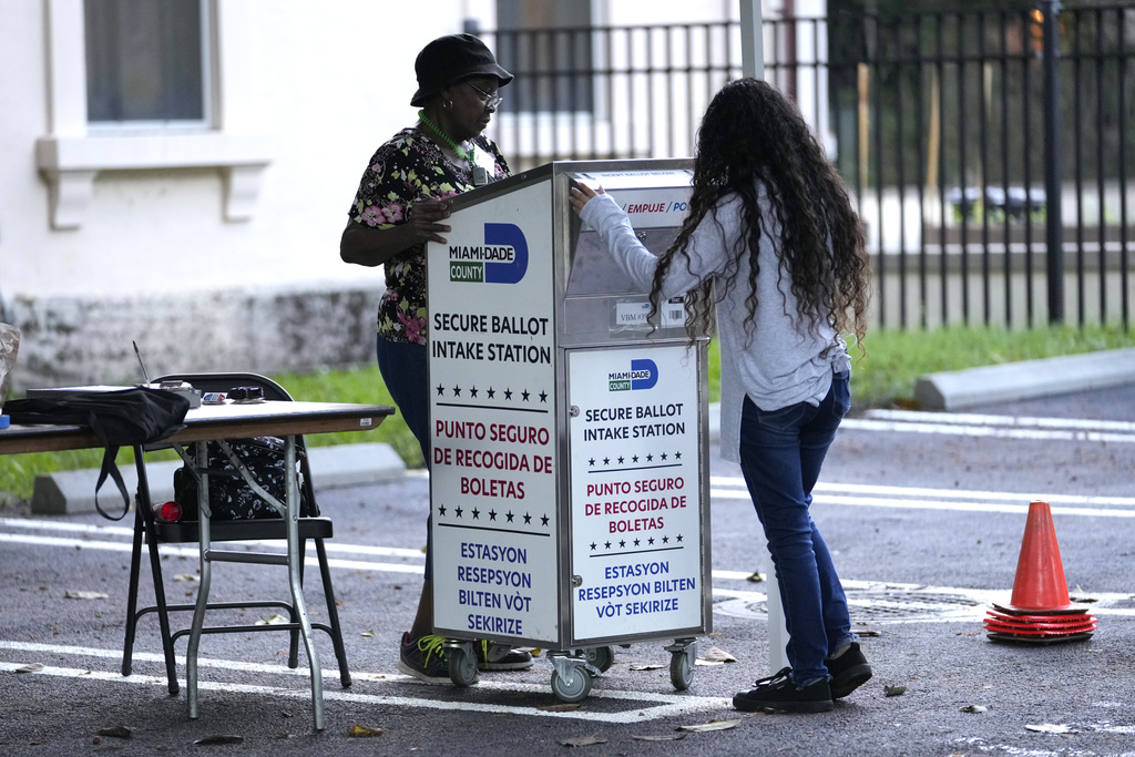 Person with long curly hair inserts ballot into ballot box in a parking lot