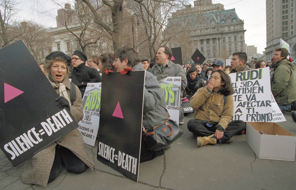 A group of protesters hold signs saying "Silence equals death" outside of New York City hall.